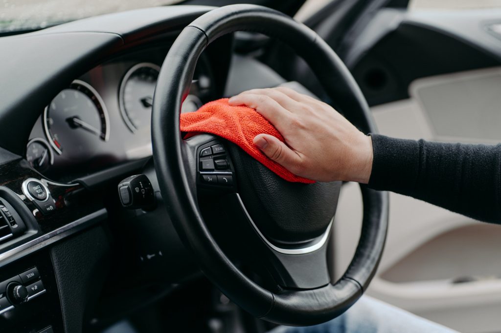 Mans hand cleaning car steering wheel with microfibre cloth